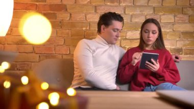 Yakın çekim portre dikkatle ev ortamında tablet ile coworking kanepede oturan genç Beyaz arkadaşlar