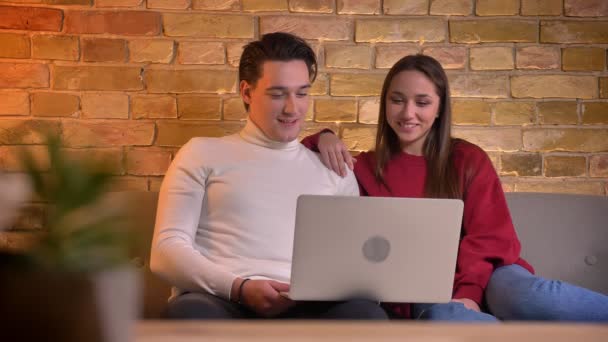 Portrait of cheerful caucasian friends watching into laptop and laughing on sofa in home atmosphere. — Stock Video