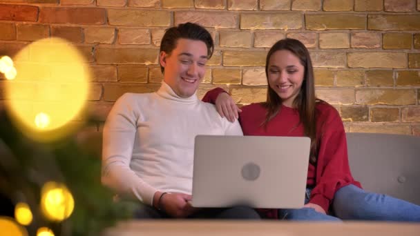 Close-up portrait of cheerful caucasian friends watching into laptop and laughing on sofa in home atmosphere. — Stock Video