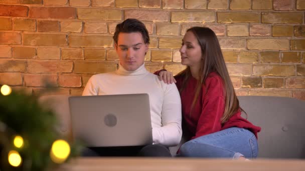 Portrait of relaxed caucasian couple watching into laptop and woman lying on man s shoulder on sofa in home atmosphere. — Stock Video