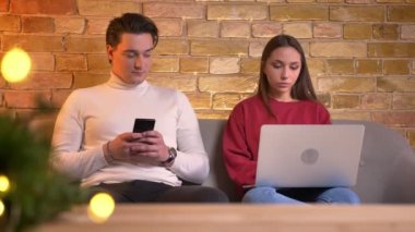 Erkek ve kadın kendi dizüstü bilgisayar ve akıllı telefon yerine koy daha da mutlu rahat ev ortamında iletişim başlangıç oturmak.