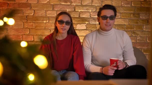 Couple caucasien en lunettes 3D assis sur le canapé et regarder un film avec tasse de boisson est choqué dans l'atmosphère de Noël . — Video