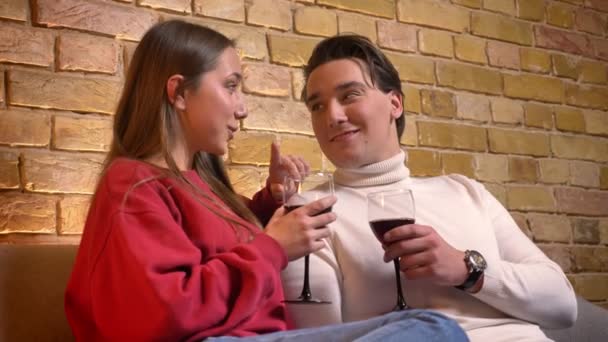 年轻的高加索夫妇的肖像坐在沙发上, 喝着葡萄酒在舒适的家庭气氛中互相交谈. — 图库视频影像