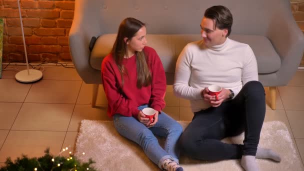 Vista de arriba hacia abajo de alegres amigos caucásicos sentados en la alfombra con té y la comunicación en el ambiente casero de Navidad . — Vídeo de stock
