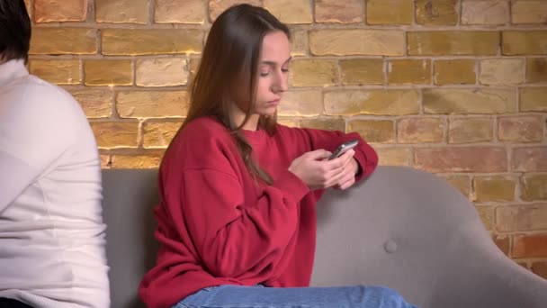 Доллі знімок молодого білоруського чоловіка і жінки, що сидить спиною на дивані зі смартфонами в домашній атмосфері . — стокове відео