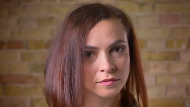 Portret van Kaukasische brown-headed vrouw negatief draaien haar hoofd en kijken in de camera op bricken muur achtergrond. — Stockvideo