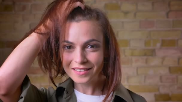 Portait de joven hermosa mujer de cabeza marrón sosteniendo su cabello y posando en la cámara sobre fondo de pared de ladrillo . — Vídeo de stock