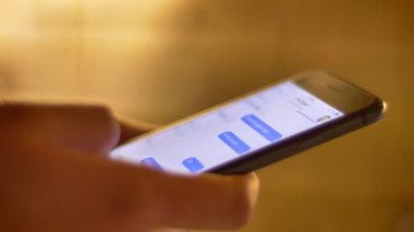 Erkek tipik smartphone üzerinde bulanık sıcak ışık arka plan kullanarak messenger içinde profil elinde kadeh yakın çekim.