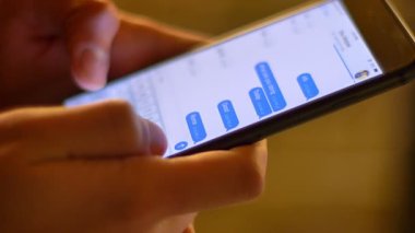 Yakın çekim çekim profil smartphone üzerinde bulanık sıcak ışık arka plan kullanarak Messenger yazarak ellerinde mans.