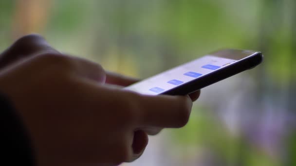 Primer plano de las manos masculinas en perfil escribiendo en messenger usando smartphone sobre fondo de luz verde borrosa . — Vídeos de Stock