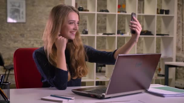 Portret van blonde Kaukasische zakenvrouw voor laptop in kantoor selfie-foto's maken met behulp van smartphone. — Stockvideo