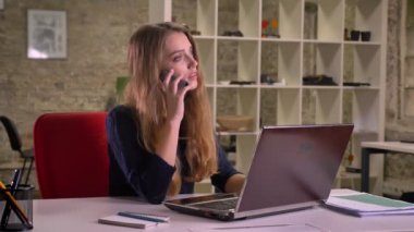 Cidden telefonda konuşurken office içinde laptop önünde özenli sarışın beyaz iş kadını portresi.