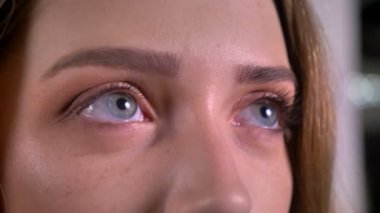 Yakın çekim portre sarışın beyaz genç kadının yukarı doğru gri arka plan üzerinde izlerken.