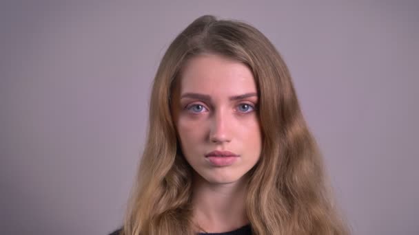 Portret van mooie blonde Kaukasische jonge vrouw serieus kijken naar de camera op een grijze achtergrond. — Stockvideo