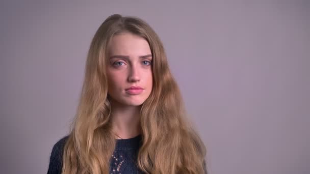 Portrait of beautiful blonde caucasian young woman watching into camera and negatively turning her head on gray background. — Stock Video