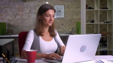 C işyeri kapalı olmak gülümser ve statisfied kahve içme dizüstü bilgisayarda yazarak çekici kadın ofis çalışanı alır