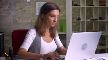 Görme yeteneğini işyeri memnuniyeti ile gülümseyerek kameraya dönüm laptop önünde oturan çekici kadın ofis çalışanı