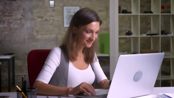 Trabalhadora de escritório atraente sentada na frente do laptop e ficando extremamente feliz quando descobre as boas notícias sobre o local de trabalho — Vídeo de Stock