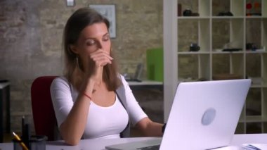 Belgili tanımlık laptop önünde oturan çekici kadın ofis çalışanı sorunu nedeniyle işyeri kapalı buolduğunun