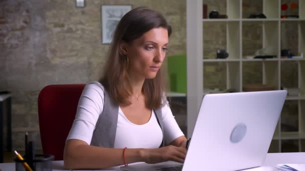 Привлекательный офисный работник печатает на ноутбуке с проблемами и головной болью — стоковое видео