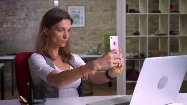 İşyeri kapalı dizüstü bilgisayar önünde oturup selfies alarak çekici kadın ofis çalışanı