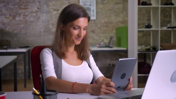 Привлекательная женщина-офисный работник просматривает планшет улыбаясь на рабочем месте в помещении — стоковое видео