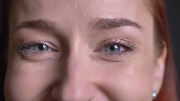 Fechar-se de olhos femininos cinzentos atraentes olhando diretamente para a câmera com uma expressão facial sorridente — Vídeo de Stock