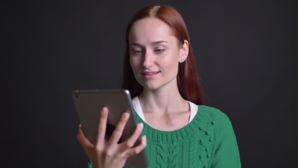 Primer plano retrato de atractiva mujer caucásica desplazándose hacia abajo en la tableta y mostrando su pantalla a la cámara sonriendo — Vídeos de Stock