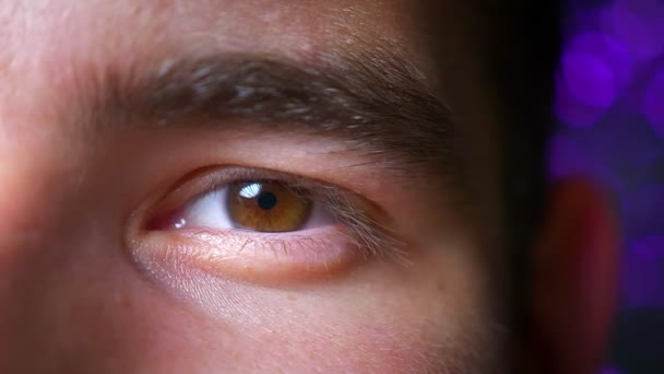 Nahaufnahme eines schönen männlichen braunen Auges, das direkt in die Kamera blickt. fröhlicher Gesichtsausdruck auf dem Hintergrund von Nachtlichtern — Stockvideo