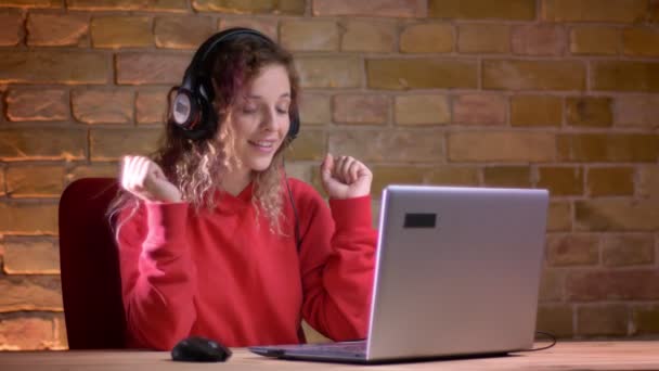 Portretul unei tinere bloggere în hanorac roșu care înregistrează video folosind laptopul pe fundal de perete de cărămidă . — Videoclip de stoc