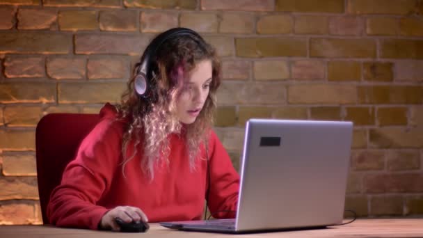 Retrato de jovem blogueira em relógios com capuz vermelho em laptop com tristeza desonrosa no fundo da parede de tijolos . — Vídeo de Stock