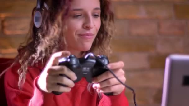 Retrato de cerca de una joven blogger jugando videojuegos usando joystick y ganando felizmente sobre fondo de pared de ladrillo . — Vídeos de Stock