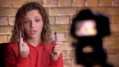 Yakın çekim portre genç güzellik blogger kayıt video kamera ve lamba bricken duvar arka plan üzerinde önünde ruj hakkında.
