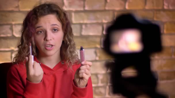 Retrato de cerca del joven blogger de belleza grabando video sobre lápiz labial frente a la cámara y la lámpara sobre fondo de pared de ladrillo . — Vídeos de Stock