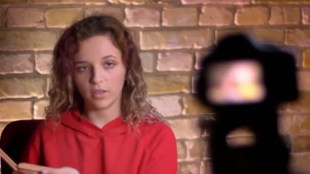 Close-up portrait of young beauty blogger recording video about powder in front of camera and lamp on bricken wall background. — Stock Video