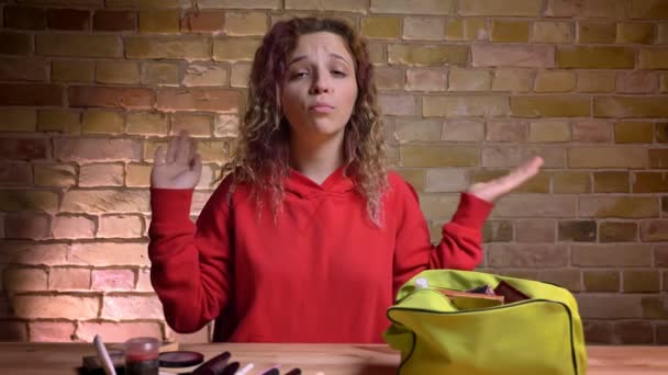 Retrato de cerca del joven blogger de belleza grabando video frente a la cámara sobre el uso de cosméticos en el fondo de la pared de ladrillo . — Vídeos de Stock