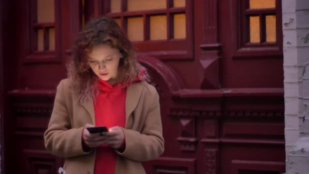 Portret van de jonge blonde Kaukasische meisje aandachtig kijken naar smartphone op wazig avond stad achtergrond. — Stockvideo