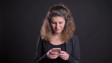 Yakın çekim smartphone izliyor ve siyah arka plan üzerine gülümseyen kilolu kafkas kadın portresi.