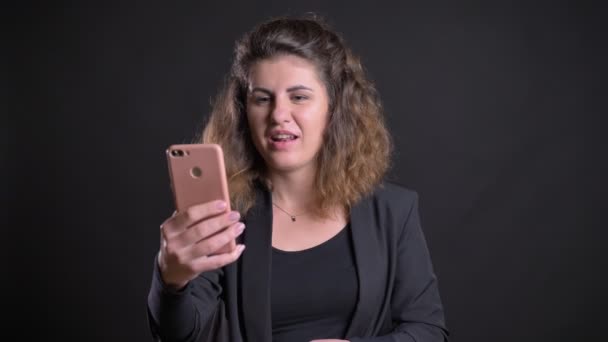 Close-up portrait of overweight caucasian woman talking in videochat using smartphone on black background. — Stock Video