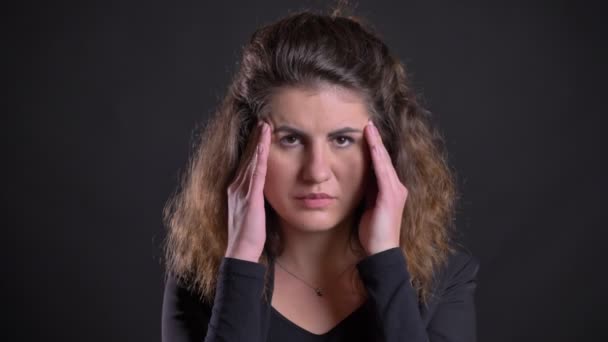 Gros plan portrait de femme caucasienne en surpoids faisant un massage à partir de maux de tête sur fond noir . — Video