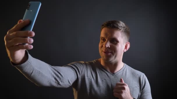 Close-up portrait of middle-aged caucasian man talking in videochat using smartphone on black background. — Stock Video