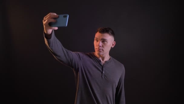 Closeup portrait of handsome caucasian fit man making selfies on the phone with the background of dark — Stock Video