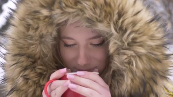 Primer plano retrato de la joven chica caucásica con taza de bebida caliente y sonriendo mirando a la cámara en el fondo de la calle de invierno . — Vídeos de Stock