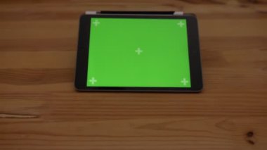 Yaklaşan yakın çekim yatay tablet ile ahşap Resepsiyon zemin üzerine yeşil perde atış.