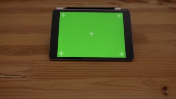 Aproximando tiro close-up de tablet horizontal com tela verde no fundo da mesa de madeira . — Vídeo de Stock