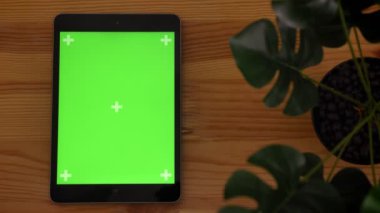 Yakın çekim üst dik tablet ile yeşil perde ahşap masa ve arka plan üzerinde bitki ile vurdu.