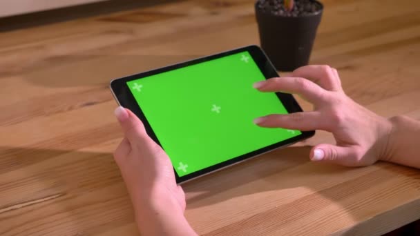水平であるタブレットと木製のデスクの背景に緑色の画面をスクロールの手のクローズ アップ ショット. — ストック動画