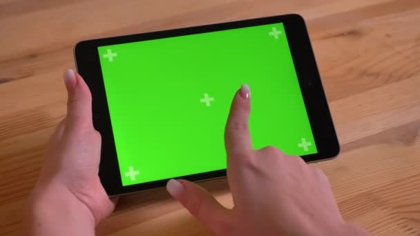 Close-up de tablet horizontal e mão feminina navegando através de tela verde no fundo da mesa de madeira . — Vídeo de Stock