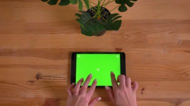 Ahşap masa ve bitki arka plan üzerinde yatay tablet yeşil ekran yazarak eller en iyi atış.
