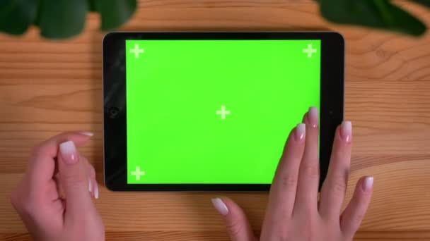 Nahaufnahme von weiblichen Händen, die den grünen Bildschirm der horizontalen Tablette auf Holztisch und Pflanzenhintergrund berühren. — Stockvideo